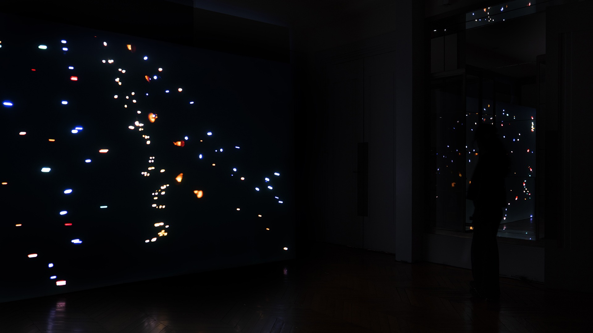 Des petites lumières de toutes les couleurs semblent tourner dans un espace noir. Il s'agit en fait d'un costume porter par une personne qui tournoie dans l'obscurité et qui fait virevolter ces petites lumières autour des visiteurs.