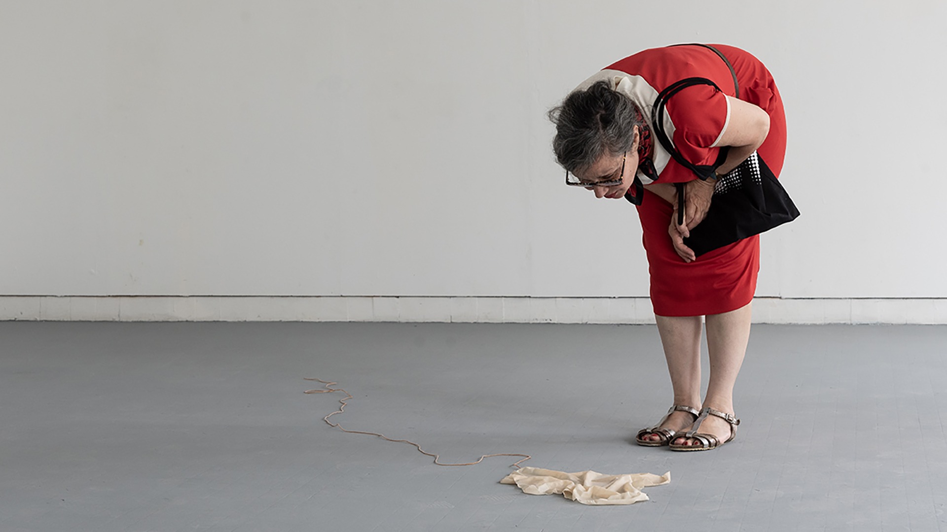 Une femme habillée en rouge est penchée sur l'oeuvre de Lilou : ce qui semble être un mouchoir, jeté au sol.