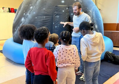 Planétarium gonflable mobile : des enfants s'apprêtent à entrer dans le dôme immersif avec un médiateur du Outreach Centre. Dispositif transportable pour découvrir l'Univers en milieu scolaire ou hospitalier.