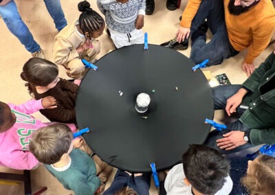 Démonstration de la maquette de l'espace-temps : enfants et adultes expérimentent ensemble les déformations gravitationnelles autour d'une toile tendue circulaire.