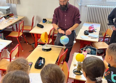 Médiation scientifique en classe : démonstration du système Terre-Lune-Soleil avec une maquette mobile. Un médiateur explique les mouvements célestes à des jeunes élèves.