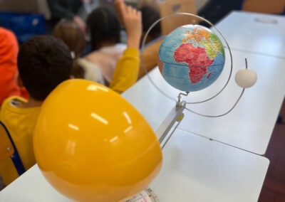 Maquette Terre-Lune-Soleil : dispositif pédagogique du Outreach Centre illustrant les mouvements célestes et les saisons. En arrière-plan, atelier de médiation avec des enfants.