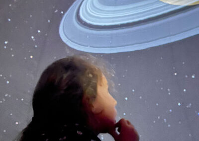 Planétarium immersif : une enfant découvre Saturne et l'Univers projetés sur la voûte du planétarium. Expérience visuelle pour explorer le cosmos et comprendre l'astrophysique.